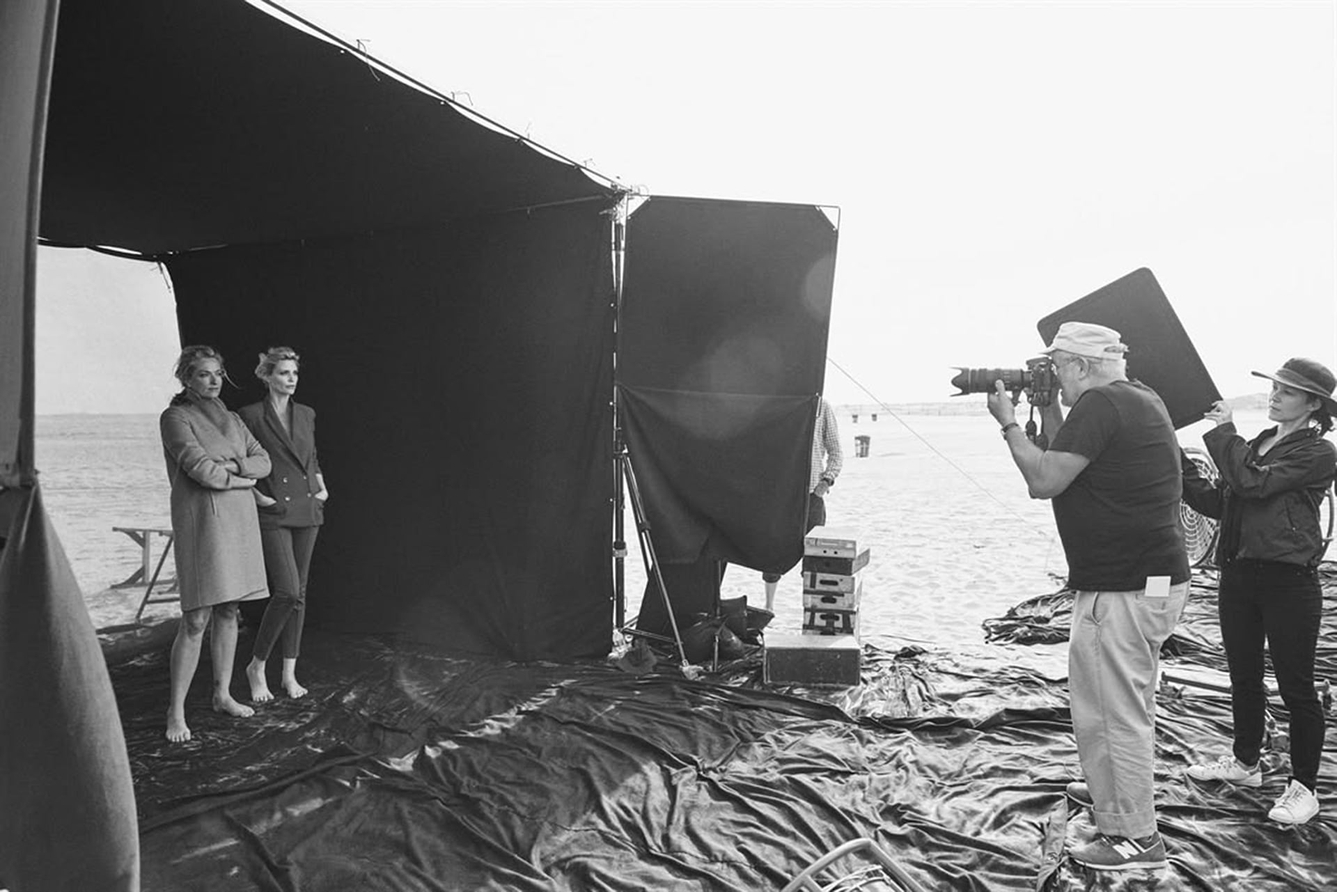 A photographer takes pictures of two models posing under a black canopy set up on a beach